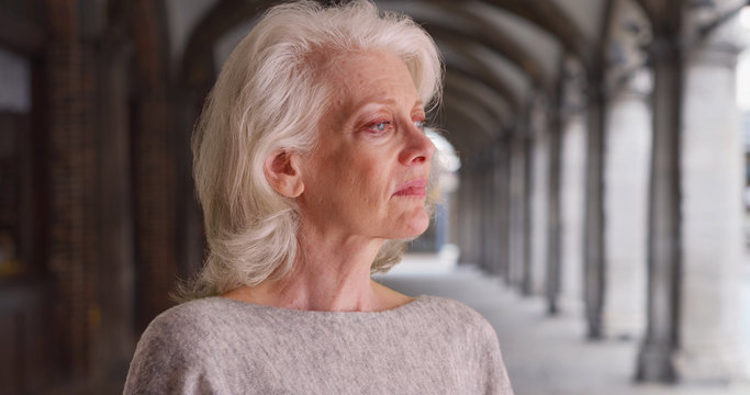 Sad Older Woman Looking Away Standing Under Archway Outdoors With Dramatic Light