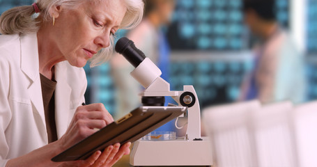 Senior woman medical researcher taking notes on tablet computer in busy lab