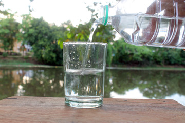 Close up pouring purified fresh drink water from the bottle on wooden table with nature background