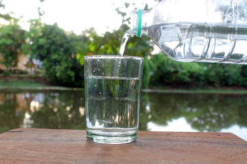 Close up pouring purified fresh drink water from the bottle on wooden table with nature background