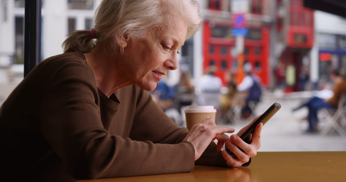 Happy senior woman shopping online with credit card and phone in coffee shop