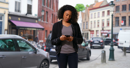 Fototapeta premium Pretty black woman walking through the city stopping to use her phone