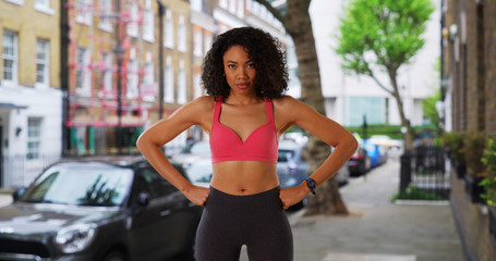 Fototapeta na wymiar Confident black female jogger in active wear standing on city street