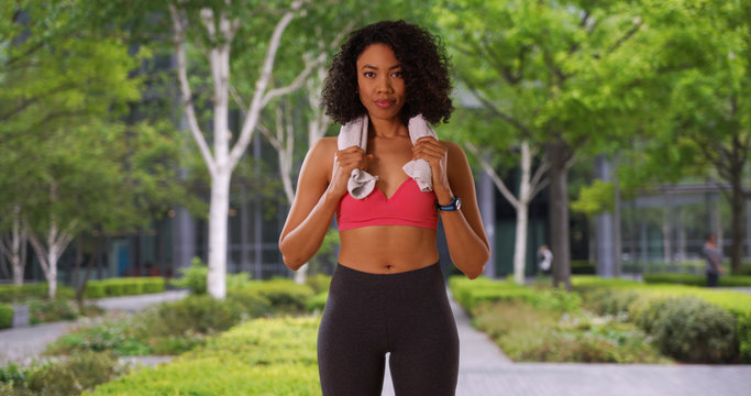 Black woman finishes working out in gym stands outside with towel around neck
