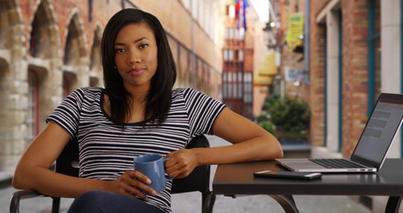 Black female outdoors with her laptop holding cup of coffee smiling at camera
