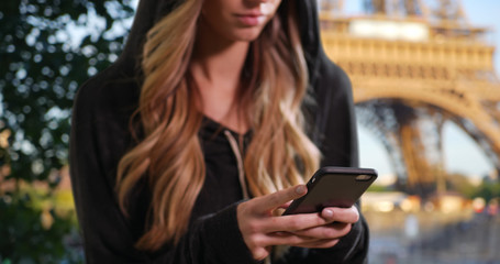 Blonde female in a hoodie texting with mobile phone in Paris