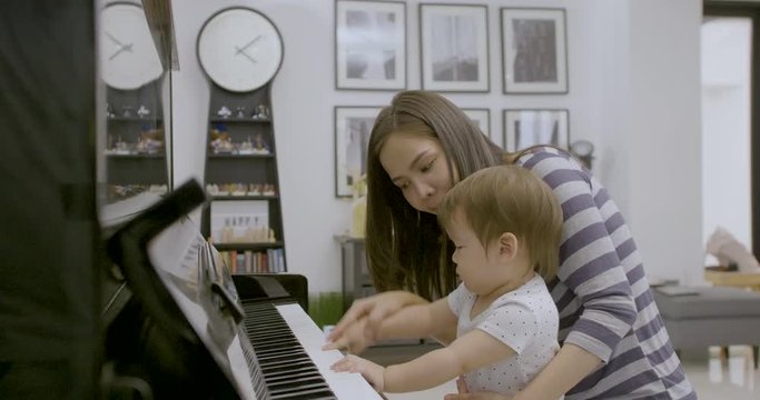 Side view of young asian mother playing piano with her baby boy.