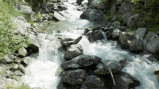 SLOW MOTION Watching a waterfall flow with blue skies and clouds in the mountains near Auron, France.