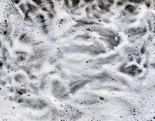 White foam and soap on dark background. Abstract pattern. The concept of washing oily pan or black...