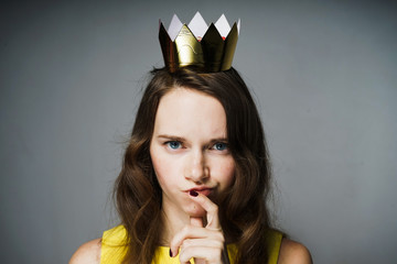 serious young girl in a yellow dress thinks about something, on her head a golden crown