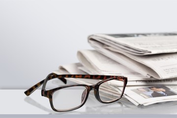 Newspapers with reading glasses on background