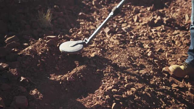 Metal Detector being held over exposed rocks by a geologist to look for gold