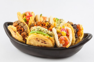Arepas with assorted fillings served in a black ceramic dish on white background