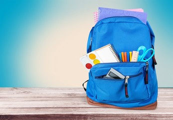 School Backpack with supplies on wooden background