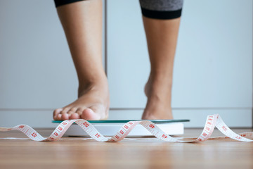 Woman foot stepping on weigh scales with tape measure,Weight loss,Body and good health concept