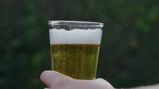 SLOW MOTION raising a glass of beer in hand with blurred background