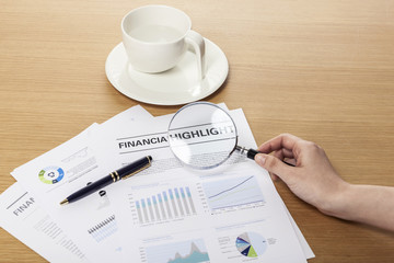 magnifier closeup with financial paper on the wood table.