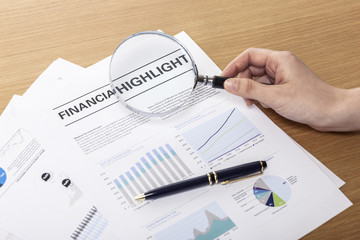 magnifier closeup with financial paper on the wood table.