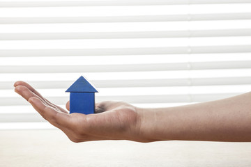 Naklejka premium woman hand hold a blue wood house at the office.