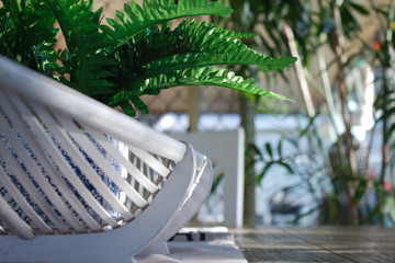 Obraz na płótnie Canvas A fake green fern house plant potted in a blue & white plant pot is placed in a white cane oval basket. The table decoration sits in the centre of a wooden dining table in a light & airy dining area.