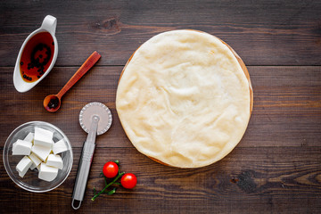 Process of cooking pizza. Pizza Margarita. Raw dough and filling. Cherry tomatoes, cheese mozzarella, spices near knife for pizza on dark wooden background top view mockup copy space