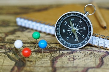 Compass, notebook and marking pins on blur vintage world map, journey concept © sundaemorning