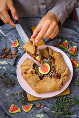 Woman hands cut, take, hold tasty delicious lean fig tart full of sweet fruits and dry fruits. Backed in oven, made for fasting days. Sweet vegan dessert, vegetarian breakfast. Healthy food. 