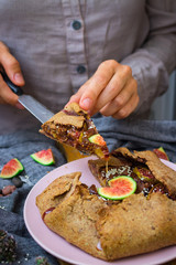 Woman hands cut, take, hold tasty delicious lean fig tart full of sweet fruits and dry fruits. Backed in oven, made for fasting days. Sweet vegan dessert, vegetarian breakfast. Healthy food. 
