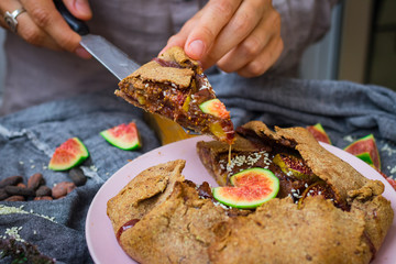 Woman hands cut, take, hold tasty delicious lean fig tart full of sweet fruits and dry fruits. Backed in oven, made for fasting days. Sweet vegan dessert, vegetarian breakfast. Healthy food. 