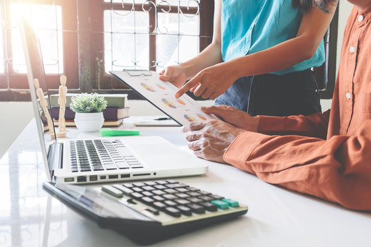 Mature business man and younger colleague using laptop and business document to discuss information on white desk table at office.Business people meeting concept.