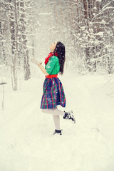 Fototapeta na wymiar brunette girl with long hair in a dress of traditional flowers of Santa's assistant - elf, spinning under the falling snow in the snowy winter forest for the new year
