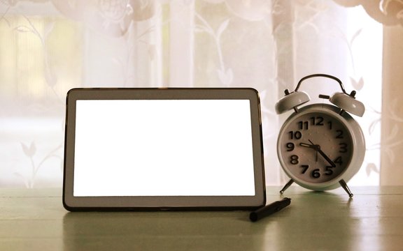 Home working desk interior blur window in morning background with white screen tablet and alarm clock on table