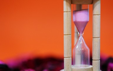 Hourglass standing on pink petals decoration closeup orange texture blur background