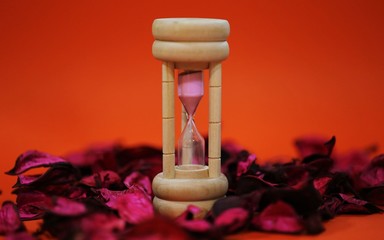 Hourglass standing on pink petals decoration closeup orange texture blur background