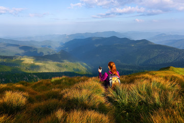 Among the nice green hummocks there is a red hair girl sitting at halt and watching the horizon with the beatufil mountains. The play of the lights and shadows. Sky with interesting clouds.