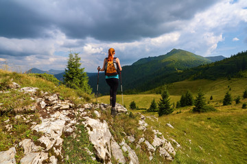 Stormy, thundery sky. The view with the peaks of mountain. Sporty red hair girl climbs up to the hill with rocks. Extreme sport. Unforgettable emotional summer day.