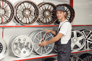 A young mechanic in uniform is standing near several tire rims