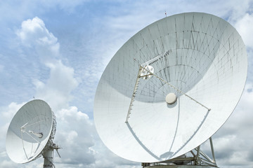 Big large white satellite dishes turn up skyward on blue sky in earth communication antenna system...
