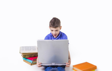 Portrait of cute teen schoolboy sitting near books and typing on laptop keyboard. Happy and surprised little boy, caucasian model isolated on white studio background. Education, study, studying