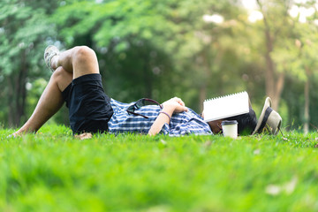 mature man sleeping on green grass in city park  with a book covers on face