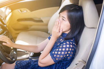 Asian woman hand holding her mouth and nose because of bad smell while driving car