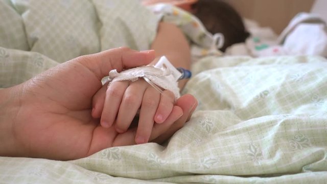 Mother holding hand of his daughter was sick in bed at the hospital.