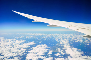 white wing of the aircraft view from airplane window seat flying in the blue sky with white clouds background over the island in the ocean, copy space, travel concept