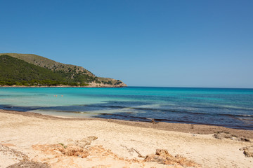 Fototapeta na wymiar View of the turquoise Mediterranean Sea and the beautiful sandy beach of Cala Agulla on the Spanish holiday island Mallorca