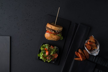 set of fast food, cheeseburger with salad and potatoes on a black background, top view