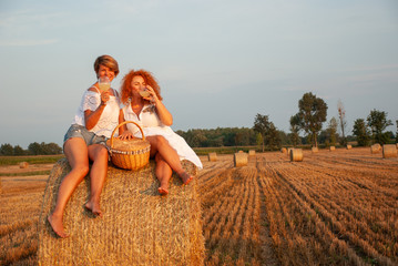 Two attractive women have picnic drink white vine and having fun on a haystack