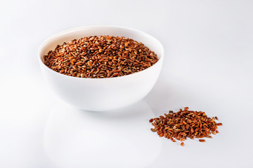 Bowl of red raw rice and a pile of rice isolated at white background.
