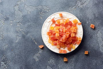 Fototapeta na wymiar Cubes of dried apricot, mango and papaya on white palte. Candied fruits over gray background.