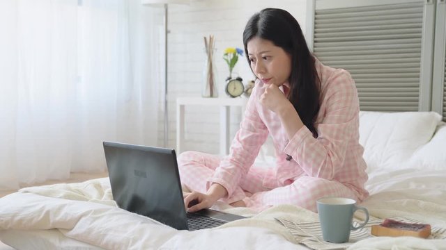 Girl typing by a laptop in the bed.