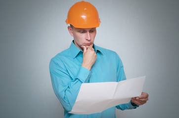 Pensive builder worker man is thinking and looking on project drafts in his hand isolated on gray background.